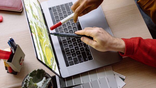 Two hands pointing pens at a laptop.