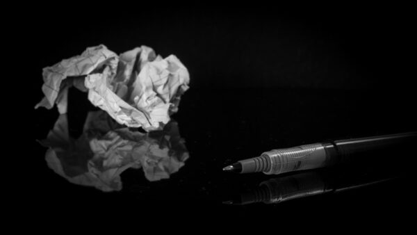 A crumpled up piece of paper next to a blank pen without a cap.