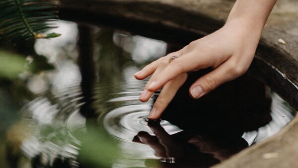 Photo of a hand dipping ring fingertip into a well full of water.