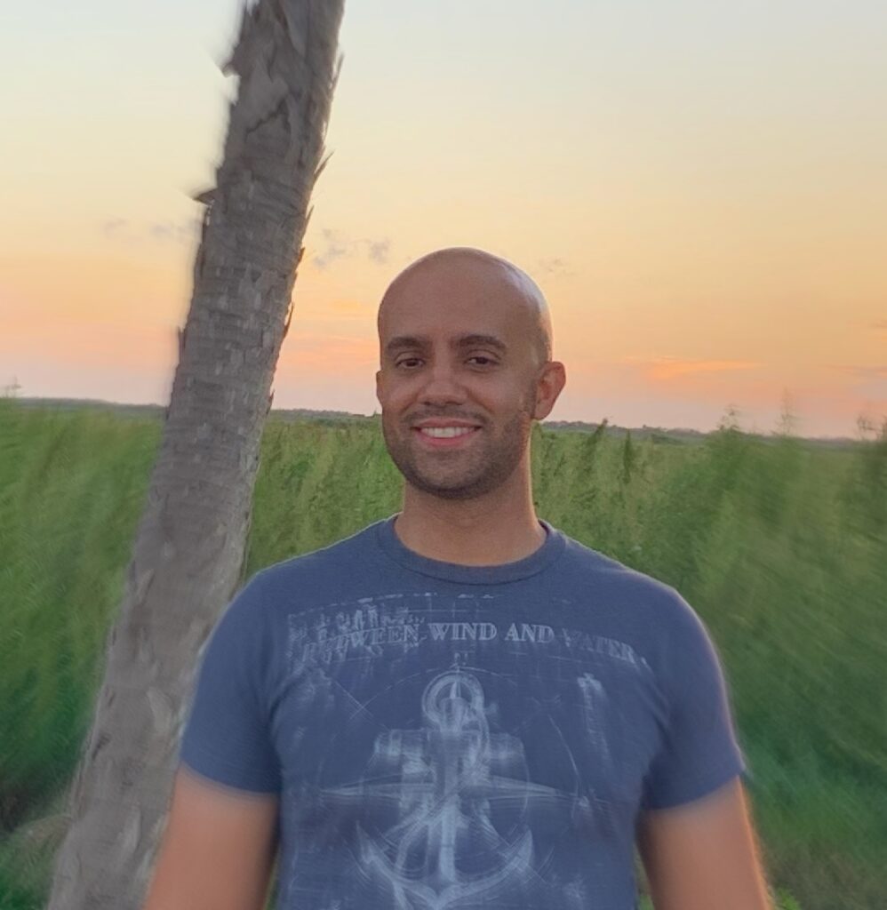 Photo of the author by a tree in a grassy field.