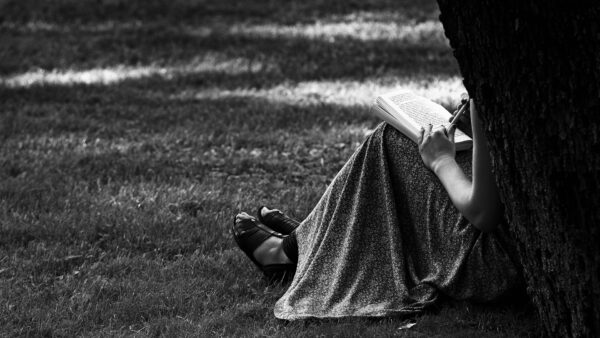 Monochrome photo of someone in a dress sitting behind a tree writing.