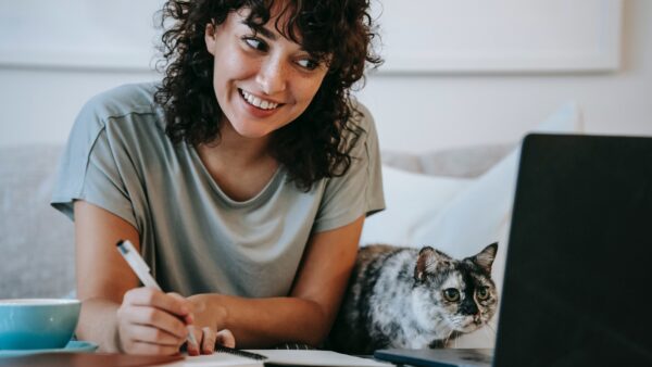 Photo of a smiling woman and a cat looking at a computer screen together.