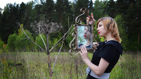 Woman expressing herself creatively with a mirror surrounded by trees.