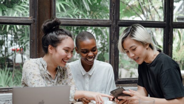 Happy multiethnic women having fun while using gadgets in a cafeteria.