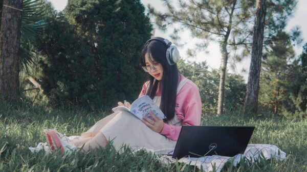 woman with headphones writing in a book in the woods.